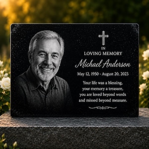Può includere: Una targa commemorativa rettangolare nera con il ritratto di un uomo sorridente con capelli grigi e barba. Il testo recita: IN LOVING MEMORY, Michael Anderson, May 12, 1950 - August 20, 2023, Your life was a blessing, your memory a treasure.