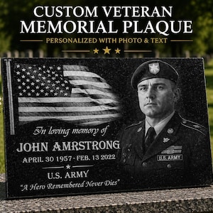 Puede incluir: Una placa conmemorativa rectangular de granito negro con un grabado de la bandera estadounidense, el retrato de un soldado uniformado y el texto: In loving memory of JOHN AMRSTRONG APRIL 30 1957-FEB. 13 2022 U.S. ARMY A Hero Remembered Never Dies.