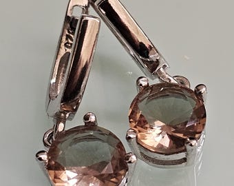 May include: A pair of silver-toned leverback earrings. Each earring features a round, faceted, peach-colored gemstone. The gemstones are set in a four-prong setting. The earrings are displayed against a light background.