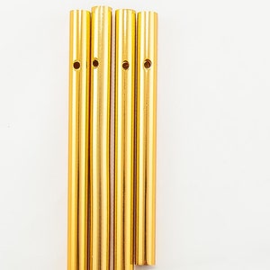 May include: Five gold metal tubes of varying lengths, each with a small hole drilled through the center. The tubes are arranged in a staggered pattern, with the longest tube at the bottom and the shortest tube at the top.