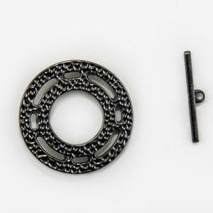 May include: A dark gray metal toggle clasp set. The round clasp has an openwork design, and the bar has a loop at one end. The jewelry finding is suitable for necklaces and bracelets.