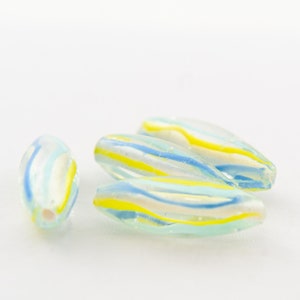 以下が含まれることがあります： 青と黄色のストライプが入ったガラスビーズが4つ。ビーズは楕円形で半透明です。