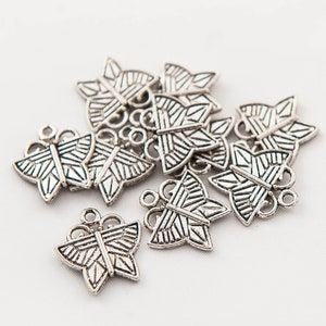 Op de afbeelding: Een groep zilveren vlinderbedels met ingewikkelde ontwerpen. De bedels hebben een lus aan de bovenkant om aan sieraden of andere knutselwerkjes te bevestigen.