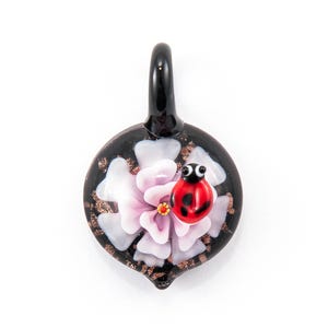 May include: A black glass pendant with a pink flower and a red ladybug on top. The pendant has gold flecks throughout.