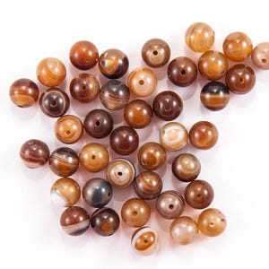 May include: A collection of brown, white, and black agate beads. The beads are round and have a smooth, polished finish.