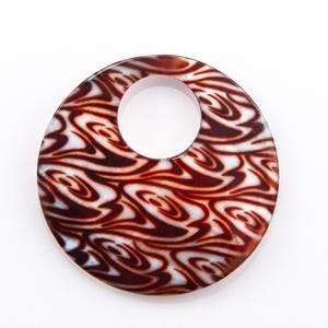 May include: A round pendant with a central hole, featuring a swirling pattern of brown and white. The pendant has a glossy finish and is set against a white background. This accessory could be used as a necklace pendant or a decorative element.