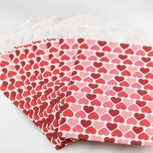 Puede incluir: Un montón de bolsas de papel con estampado de corazones rojos y rosas. Las bolsas están dobladas en forma de abanico y están listas para usar.