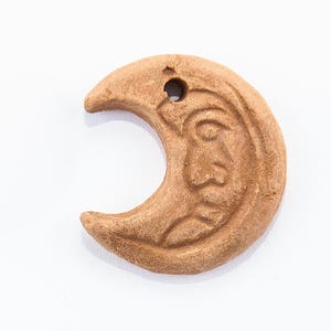 Puede incluir: Un colgante de color marrón en forma de media luna con una cara tallada en el centro.