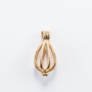 Puede incluir: Colgante de jaula de metal dorado diseñado para contener una perla u otro objeto pequeño. La jaula tiene forma de lágrima y tiene un bucle en la parte superior para sujetarlo a una cadena o cordón.