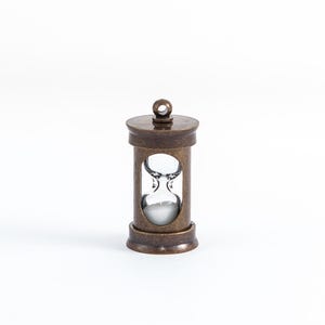 May include: A small, antique-looking brass hourglass pendant with a clear glass bulb and white sand. The hourglass is about 2 inches tall.