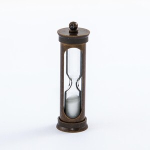 May include: A small brass hourglass with a clear glass bulb. The hourglass is filled with white sand and has a brass top and bottom.