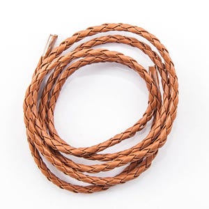 May include: A coiled, braided leather cord in a warm brown hue. The cord is tightly woven, creating a textured surface. The ends of the cord are visible, showing a smooth, unfinished edge. The cord is likely used for crafting or jewelry making.