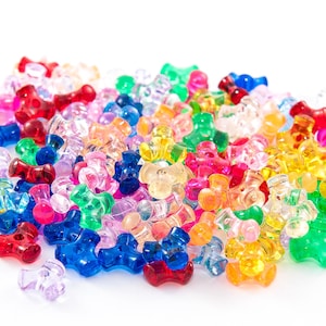 May include: A pile of colorful, translucent plastic beads in various shapes. The beads are in shades of red, pink, blue, green, yellow, and orange. They are scattered on a white surface.