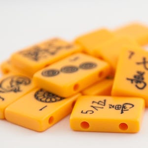 Puede incluir: Un mont&oacute;n de fichas de mahjong de color naranja con caracteres y s&iacute;mbolos chinos negros. Las fichas est&aacute;n dispuestas en un orden aleatorio.