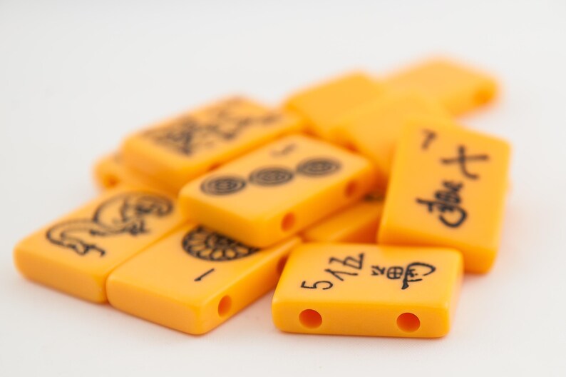 Puede incluir: Un mont&oacute;n de fichas de mahjong de color naranja con caracteres y s&iacute;mbolos chinos negros. Las fichas est&aacute;n dispuestas en un orden aleatorio.