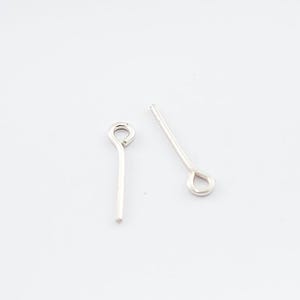 May include: Two silver-toned head pins with a loop at the top. The pins are straight and have a smooth finish.