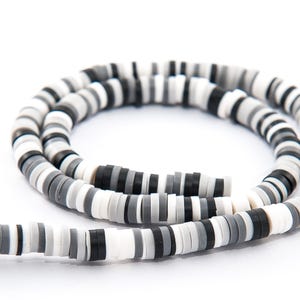 May include: A necklace made of small, flat, round beads in black, white, and grey. The beads are strung together, creating a flexible strand. The necklace is shown against a white backdrop.
