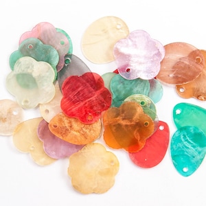 Może przedstawiać: Zestaw kolorowych, przezroczystych plastikowych kwiatów i owalnych kształtów z otworami do nawlekania. Kształty są w odcieniach zieleni, czerwieni, różu, pomarańczy i żółci.