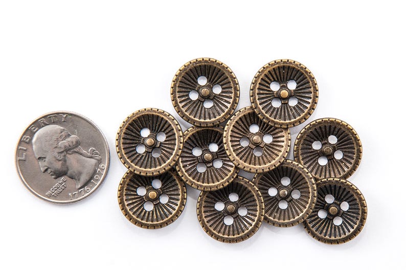 May include: A collection of antique brass-colored buttons with a radial design and four holes, next to a U.S. quarter coin. The buttons have a vintage aesthetic and are arranged on a white surface.