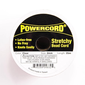 May include: A spool of clear stretchy bead cord, 2mm in size and 25m in length. The label reads "POWERCORD® Stretchy Bead Cord" and lists features: Latex-free, No Fray, Knots Easily. It also includes a warning: "CAUTION: NOT A TOY, NOT INTENDED FOR USE BY, OR IN PRODUCTS INTENDED FOR CHILDREN 14 OR UNDER. MAY BE HARMFUL IF SWALLOWED."