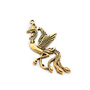 Puede incluir: Colgante de fénix dorado antiguo detallado. El ave se representa con las alas extendidas y plumas de la cola fluidas. El colgante tiene un pequeño lazo en la parte superior para sujetarlo a una cadena u otro componente de joyería.