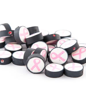 May include: A pile of black and white round beads with pink ribbon designs. The beads are about 1 inch in diameter.