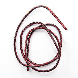 Puede incluir: Cordón de cuero trenzado rojo y negro sobre fondo blanco. Este cordón, probablemente para bisutería o artesanía, está hecho de hebras entrelazadas, creando una apariencia texturizada.