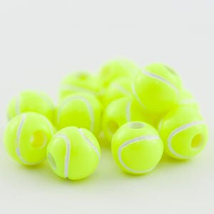May include: A group of yellow tennis ball-shaped beads with white stitching. The beads are arranged in a pile on a white surface.