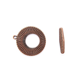 May include: A copper-colored metal pendant with a circular design. The pendant has a textured surface with a radial pattern. The pendant has a small loop at the top for attaching a chain or cord.