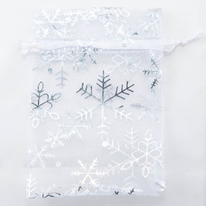 May include: White organza gift bag with a silver snowflake pattern. The bag has a drawstring closure.