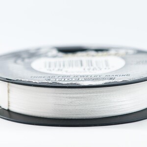 Może przedstawiać: Szpula białej nici do tworzenia biżuterii. Szpula jest oznaczona "Thread for Jewelry Making" i "Spider Wire".