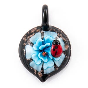 May include: A black glass pendant with a blue flower and a red ladybug on top. The pendant has a gold glitter finish.