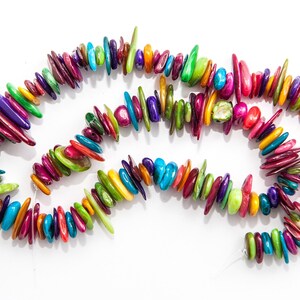 Puede incluir: Un collar vibrante compuesto por cuentas de colores de forma irregular. Las cuentas son en tonos de rojo, morado, verde, azul y amarillo. El collar se muestra sobre un fondo blanco, mostrando su diseño brillante y juguetón.