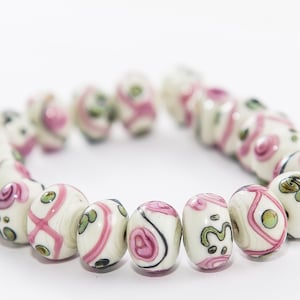 May include: A strand of white and pink beads with floral patterns. The beads are round and have a glossy finish.