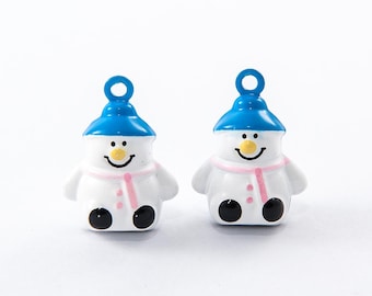 Könnte beinhalten: Zwei schneemannförmige Ornamente. Jeder Schneemann hat einen weißen Körper, eine blaue Mütze und einen rosa Schal. Sie haben schwarze Augen und Füße sowie eine gelbe Nase und einen lächelnden Mund. Die Ornamente haben oben eine Schlaufe.