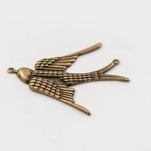 May include: A gold-toned metal swallow charm with detailed wings and a loop at the top for attaching to jewelry or crafts.