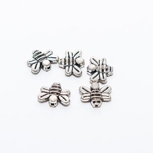 Può includere: Sei ciondoli a forma di ape argentati con un design dettagliato. I ciondoli sono perfetti per la creazione di gioielli o per aggiungere un tocco di fantasia ai lavori artigianali.