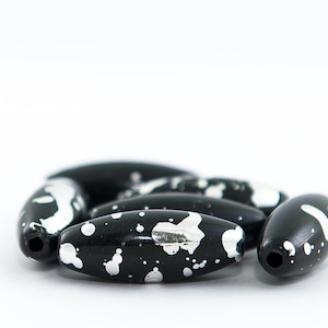 以下が含まれることがあります： 斑点模様の黒と銀の楕円形のビーズのグループ。