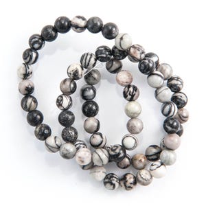 Puede incluir: Tres hebras de cuentas redondas rayadas en blanco y negro, cada hebra es una pulsera.