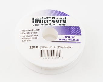 May include: A spool of clear nylon monofilament called "Invizi-Cord" for jewelry making. The spool is white with purple text and a barcode. It is 328 feet (100 meters) long and 0.01 inches (0.25 millimeters) in diameter.