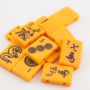 May include: A close-up of a pile of yellow mahjong tiles with black Chinese characters and symbols. The tiles are arranged in a random order.