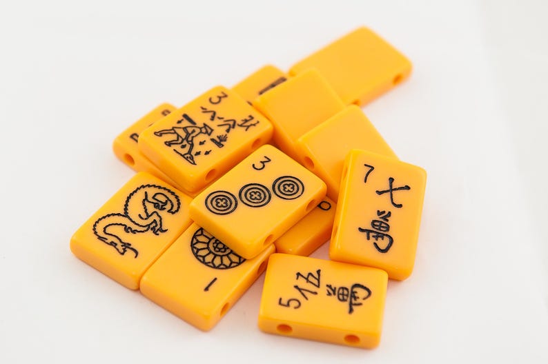 Puede incluir: Primer plano de un mont&oacute;n de fichas de mahjong amarillas con caracteres y s&iacute;mbolos chinos negros. Las fichas est&aacute;n dispuestas en un orden aleatorio.