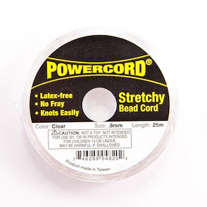Könnte beinhalten: Eine Spule mit klarem, dehnbarem Perlenband, beschriftet mit "POWERCORD Stretchy Bead Cord". Das Etikett zeigt außerdem "Latex-frei, No Fray, Knots Easily", "Color: Clear", "Size: 0,8 mm", "Length: 25 m" und "Product made in Taiwan".