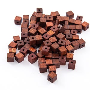 Puede incluir: Un montón de pequeñas cuentas cuadradas de madera de color marrón oscuro. Cada cuenta tiene un agujero cuadrado en el centro. Estas cuentas son ideales para la fabricación de joyas y otros proyectos de artesanía.