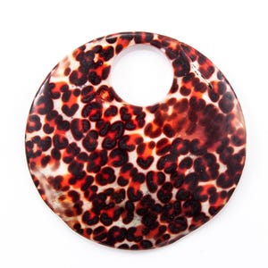 May include: A round, patterned pendant with a hole at the top. The pendant features a tortoiseshell design with brown and black spots on a light background. The pendant is likely made of resin or a similar material.