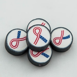 May include: Five round black and white ceramic beads with a red and blue ribbon design. The ribbon is in the shape of a figure eight and has a pattern of stars.