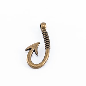 Peut inclure: Un charme en forme de crochet de pêche en métal doré avec un design détaillé. Le crochet est incurvé et a une extrémité pointue. C'est un charme populaire pour la fabrication de bijoux et l'artisanat.