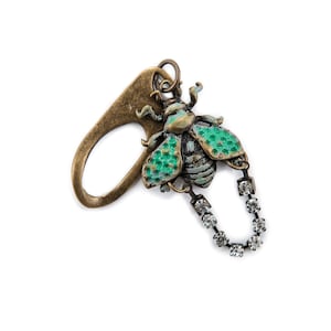 Può includere: Un ciondolo in metallo dorato con un'ape in smalto verde e blu e una catena di cristalli.