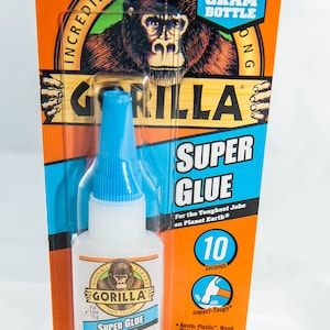 May include: A 15-gram bottle of Gorilla Super Glue with a blue cap. The bottle is labeled "Impact-Tough" and says it bonds plastic, wood, metal, ceramic, rubber, leather, paper, and more. The glue dries in 10 seconds.