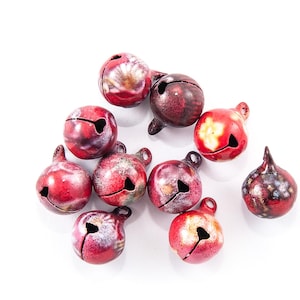 Peut inclure: Un ensemble de petites cloches rondes dans des tons de rouge, bordeaux et blanc. Chaque cloche a une fente et une boucle pour la suspension. Les cloches sont regroupées sur fond blanc.